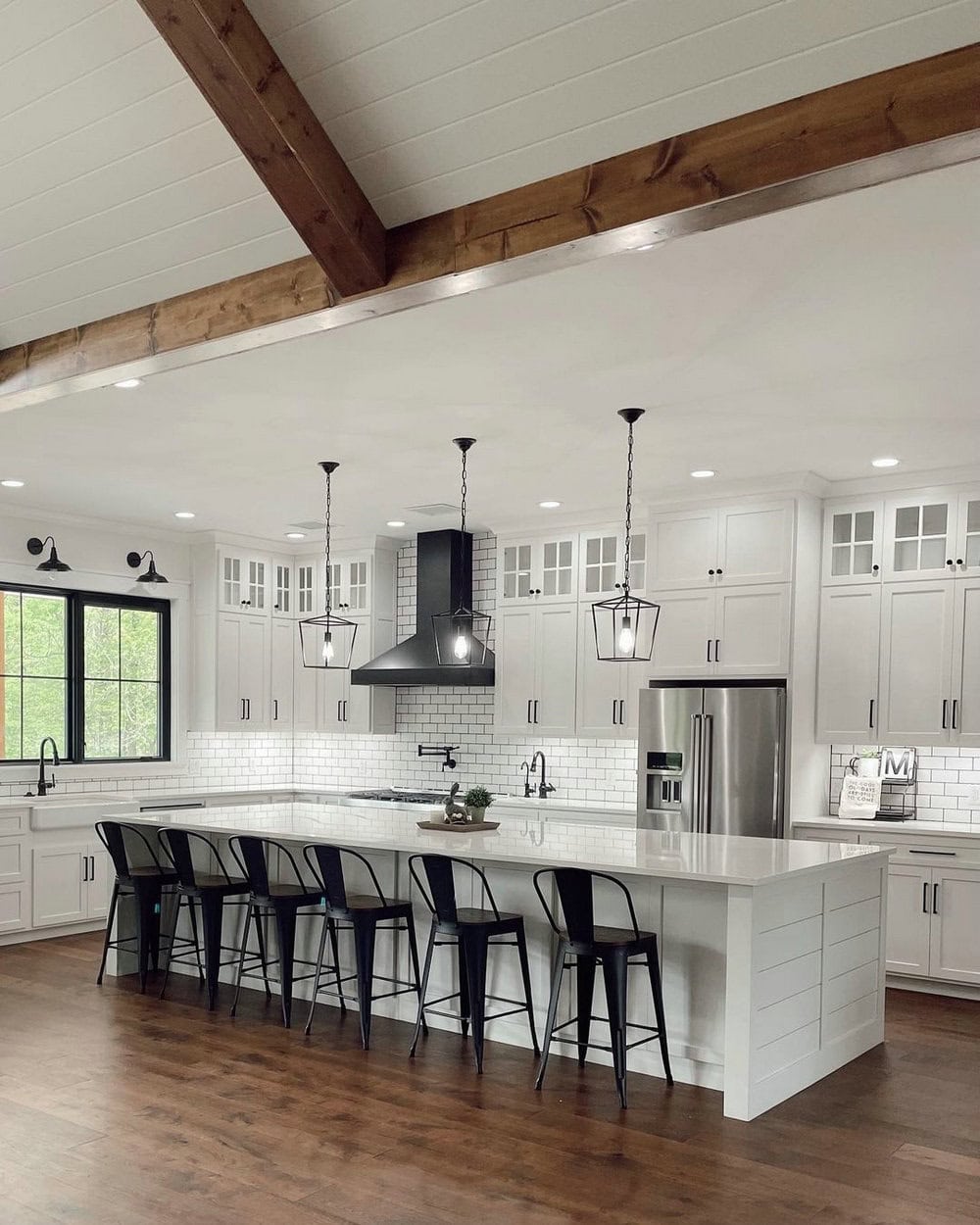 A modern farmhouse style kitchen has wood floors to seamlessly match its ceiling beams