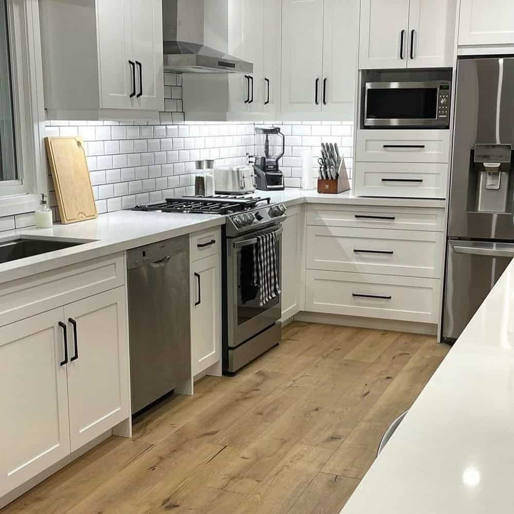 Custom white kitchen cabinets with dramatic black pulls are made complete with brown wood floors