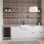 Bright kitchen featuring a glass tile backsplash, white cabinets, and open wooden shelves with potted plants.