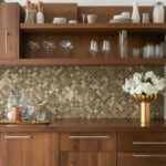 Modern kitchen with peel and stick tile backsplash, wooden cabinets, and glassware display.