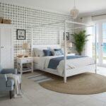 Bright bedroom featuring white and blue textiles, with a patterned tile accent wall and a view of the ocean through glass doo.