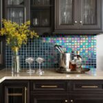 Vase with yellow flowers, glassware, and a pot with utensils on a marble countertop.