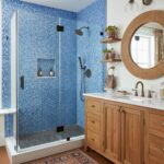 A modern bathroom featuring a glass tile shower with blue mosaic tiles, a wooden vanity, and decorative accessories for a sty.