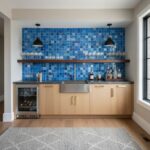 Blue glass tile backsplash in modern kitchen with wooden cabinets and black pendant lights.
