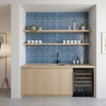 Blue glass tile backsplash with wooden shelves and mini fridge in a modern kitchen nook.