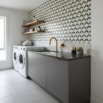 Bright laundry room with patterned geometric tiles, gray cabinetry, and gold fixtures. Modern, functional space with natural.