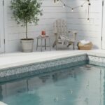 A peaceful outdoor space featuring a swimming pool with glass mosaic tiles, a wooden chair, potted plant, and string lights f.