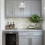 A modern kitchen featuring a shell tile backsplash with mother of pearl, complemented by gray cabinets and a glass vase with.
