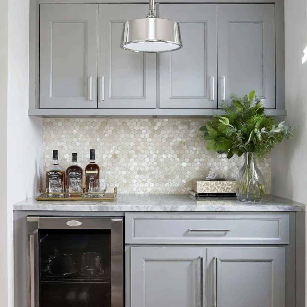 A modern kitchen featuring a shell tile backsplash with mother of pearl, complemented by gray cabinets and a glass vase with.