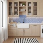 Kitchen with blue glass tile backsplash, white farmhouse sink, and light wood cabinetry.