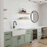 A modern kitchen featuring a white farmhouse sink, mint green cabinets, and a glass mosaic tile backsplash with open wooden s.