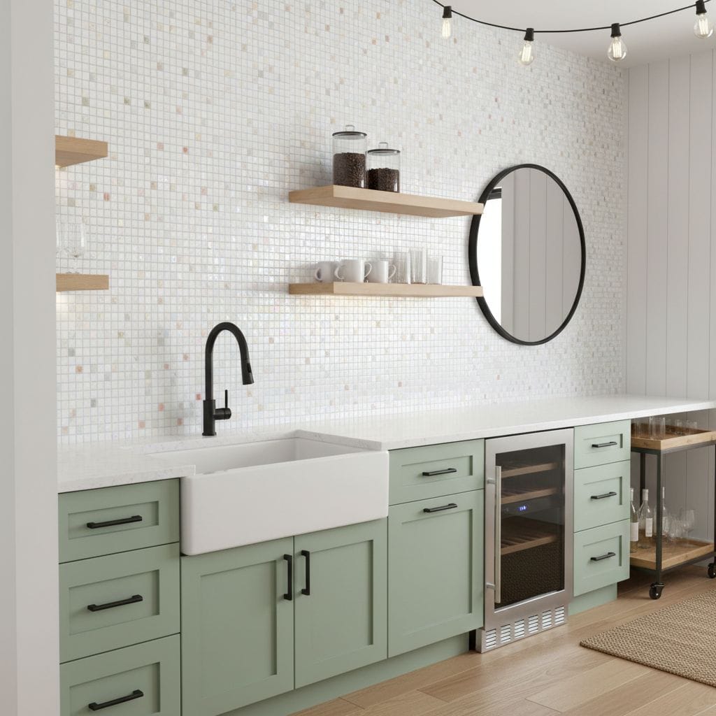 A modern kitchen featuring a white farmhouse sink, mint green cabinets, and a glass mosaic tile backsplash with open wooden s.