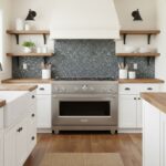 A modern kitchen featuring peel and stick tile backsplash with gray mosaic tiles, white cabinetry, and wooden open shelves.