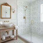 Geometric patterned tile, white with gold accents, in a bright bathroom with brass fixtures and a glass shower.