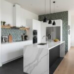 White and black kitchen with geometric patterned backsplash and sleek marble island. Features stainless steel appliances and.