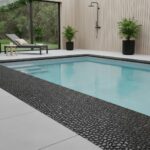 A close-up of black pebble stones used as a border around a swimming pool, creating a textured, natural look.