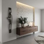 A modern interior featuring a textured shell tile wall with a floating wooden console, vase with flowers, and decorative ligh.