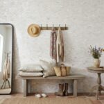 A cozy entryway with a wall decorated in mother of pearl shell tiles, featuring a bench, hat, scarves, and a vase with flower.