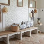 A cozy entryway featuring a wall with mother of pearl shell tiles, complemented by a wooden bench, hats, and decorative pillo.
