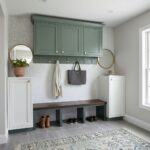 A stylish entryway featuring a shell tile wall with mother of pearl accents, complemented by white cabinets, a dark wood benc.