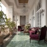 Bright sunroom with white marble walls, glass windows, and a patterned green tile floor. Features luxurious velvet furniture.