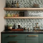 Decorative tile wall with geometric pattern in shades of green, gray, and white, featuring glassware and wooden shelves in a.