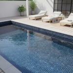Pool with glass mosaic tile and poolside lounge chairs, modern outdoor space.
