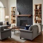 A cozy living room featuring a black textured stone fireplace, surrounded by built-in wooden shelves with decorative vases an.