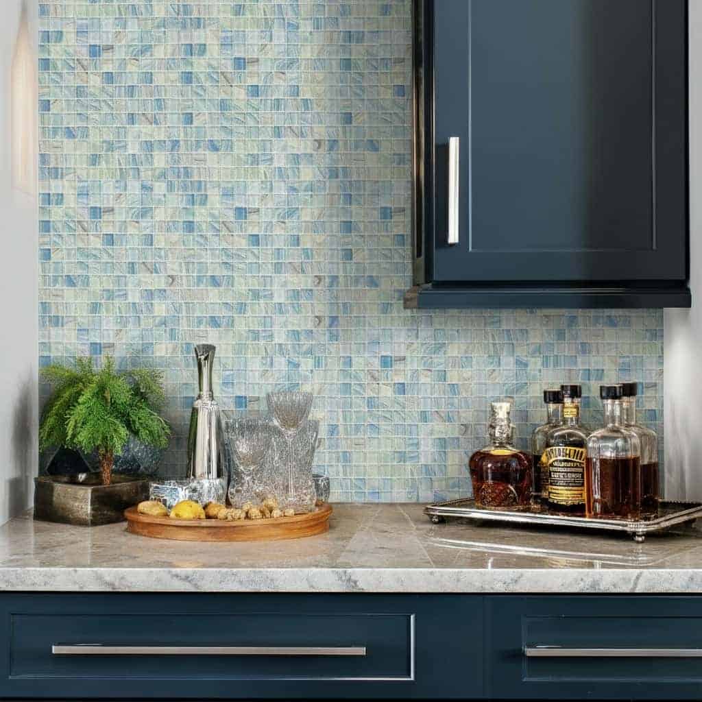 Modern kitchen with blue glass tile backsplash, countertop with drinks and decor, navy cabinets, and a sleek design.