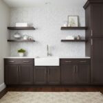Dark wood kitchen cabinets with white farmhouse sink and decorative wall shelves.