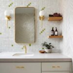 A modern bathroom featuring a mirror with shell tile accents, gold fixtures, and wooden shelves with toiletries and towels.