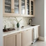 Glass tile backsplash, beige kitchen, modern design, black faucet, white countertop, glassware display.