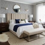 Elegant bedroom with beige upholstered bed, navy and white bedding, geometric wallpaper, and modern decor accents.