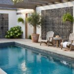 Relaxing outdoor pool area with glass tile backsplash, potted plants, and lounge chairs.