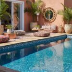 A relaxing outdoor space featuring a swimming pool with vibrant glass mosaic tiles, surrounded by tropical plants and cozy se.