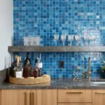 A vibrant blue glass tile backsplash in a contemporary kitchen, paired with a dark countertop, gold faucet, and decorative gl.