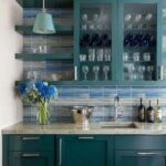 A modern kitchen featuring a blue glass tile backsplash, glass mosaic tiles, and glassware stored in glass-front cabinets.