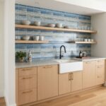 Kitchen featuring a stylish blue glass tile backsplash, white farmhouse sink, and open wooden shelves.
