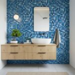 Blue glass tile backsplash in modern bathroom with wooden vanity and mirror.