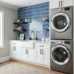 Blue glass tile backsplash behind laundry sink with white cabinets and open shelves.