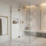 Elegant white marble tile with subtle veining, complemented by gold fixtures and a clear glass shower enclosure.