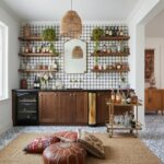 Bright kitchen with checkered tile backsplash, wooden cabinets, and open shelving with bottles and decor.