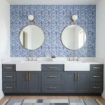 Mirror reflection of bathroom with blue glass mosaic tile backsplash and double sinks.