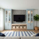 Bright living room with peel and stick tile backsplash behind TV, flanked by light blue cabinets and a potted plant.