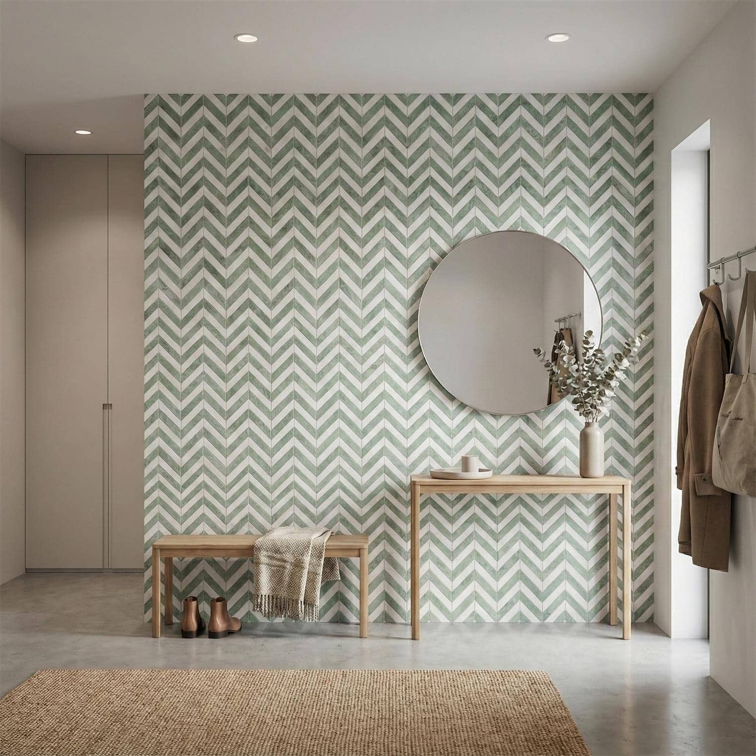 Green and white chevron patterned tile wall with a round mirror, wooden bench, and decorative vase in a modern entryway.