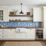 Blue glass tile backsplash in a modern kitchen with white cabinets and wooden countertops.