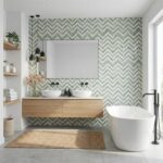 Bright bathroom with green chevron patterned tiles, white freestanding bathtub, and wooden vanity. Elegant and fresh design w.
