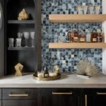 Blue glass mosaic tile backsplash with decorative glassware and bottles on wooden shelves.