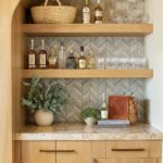 Up of a home bar with peel and stick tile backsplash, bottles, glasses, and decorative items on wooden shelves.