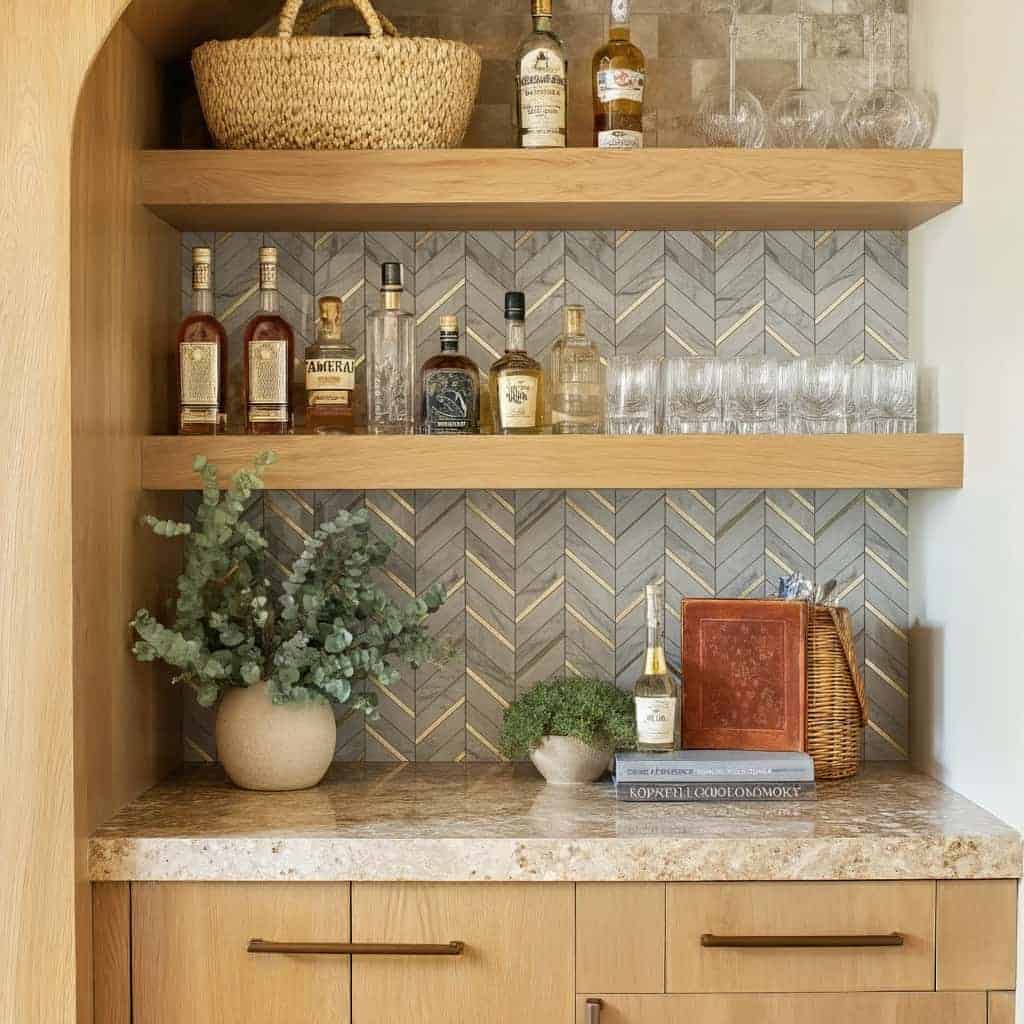 Up of a home bar with peel and stick tile backsplash, bottles, glasses, and decorative items on wooden shelves.